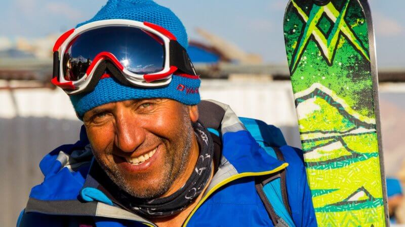 An skier with ski goggles on his head smiles for the camera.