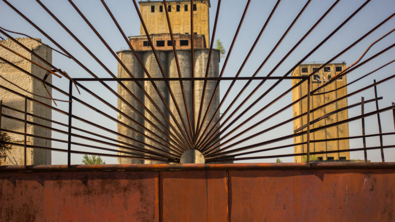 Two abandoned factory towers behind a rusty fence.