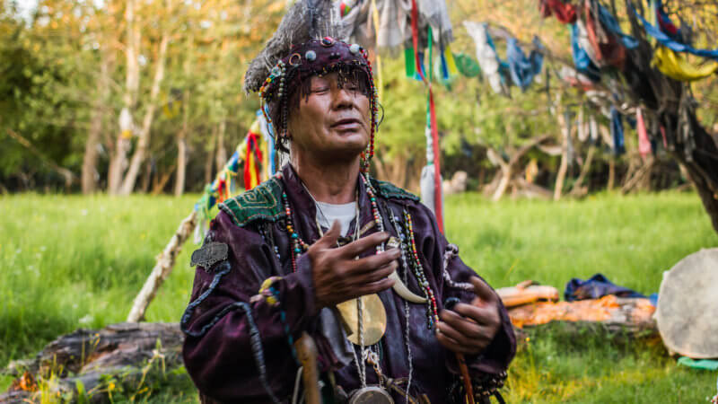 A shaman in traditional clothes with his eyes closed speaking to the forest spirits.