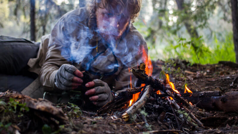 A close up photo of an adventure huddled in the dirt and making a fire.