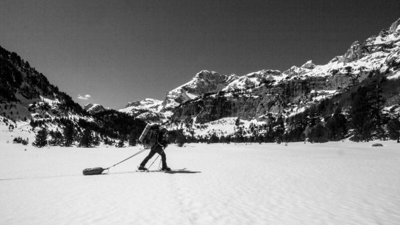 Black and white photo of skier walking past camera and towing bag.