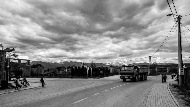 Black and white photo of a truck driving as kids walk to school.