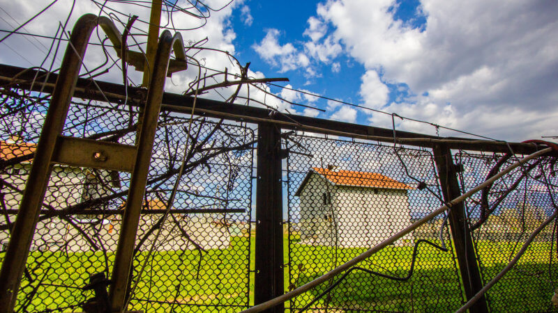 Barbed wire and metal fence framing a Kosovo farm.