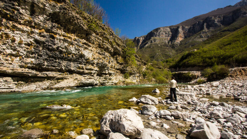 Albanian alpine river valley with man fishing.