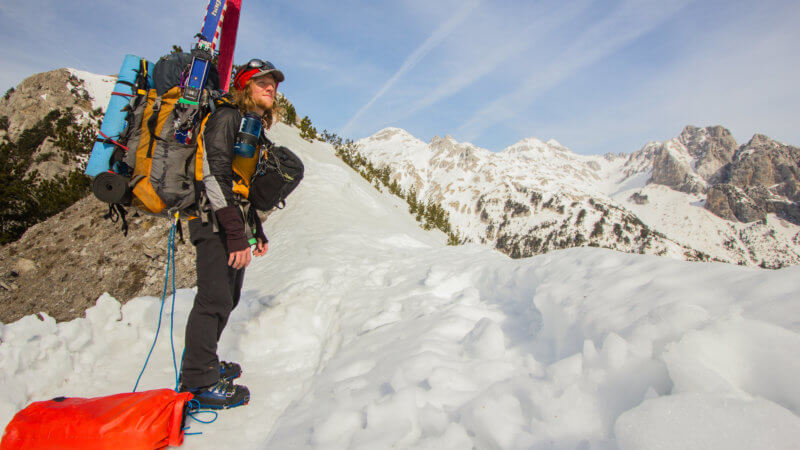 A solo skier with heavy bag stands on top of a mountain pass.