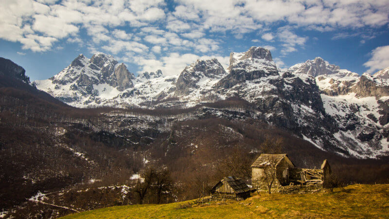 Rugged-looking Albanian farm with snowy Dinaric Alps in background.