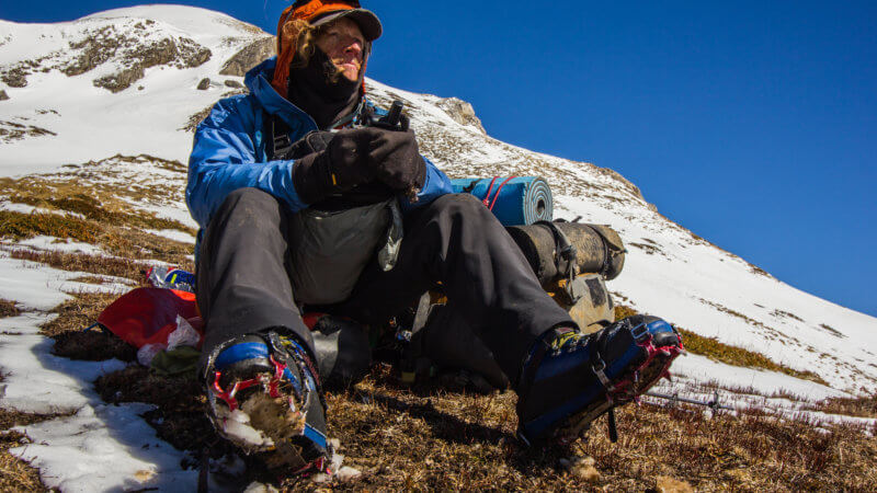 A hiker sitting on ground with crampons on feet.