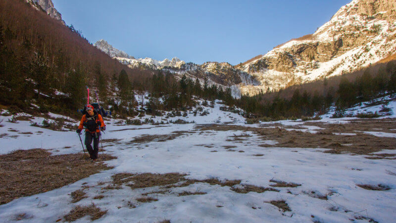 Lone hiker with skis hiking through snowy valley in Peaks of the Balkans Trail.