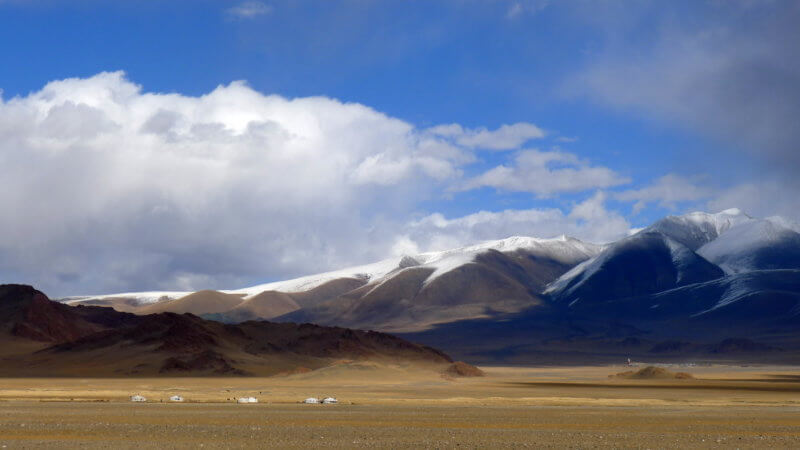 A landscape photo of snowy hills and a flat plateau with a few gers in the distance.