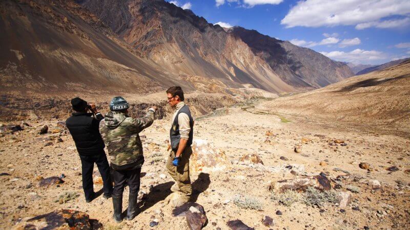 Three men looking down into a long and uninhabited valley in Tajikistan.