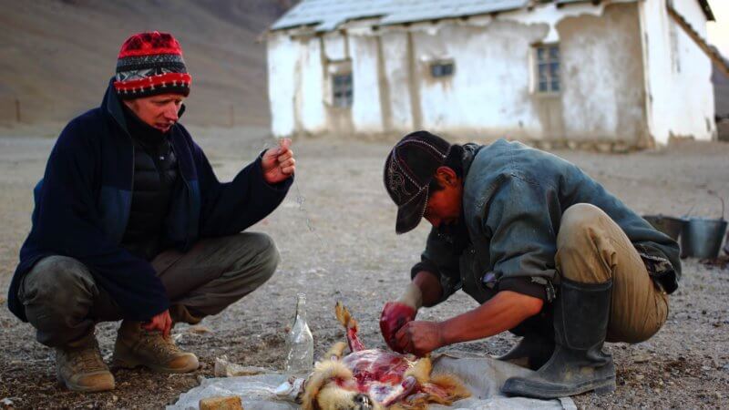 Two men huddled over the remains of a marmot that's been caught for its meat.