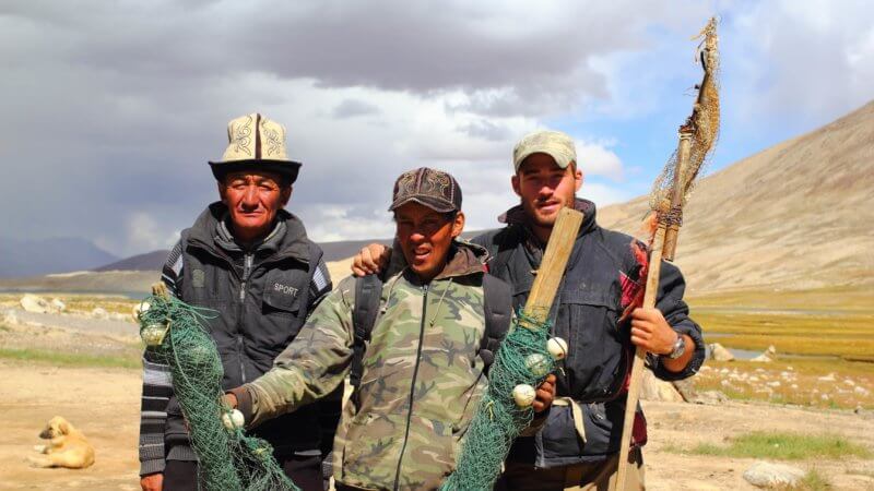 Three men holding up archaic, homemade fishing nets used for mountain fishing.
