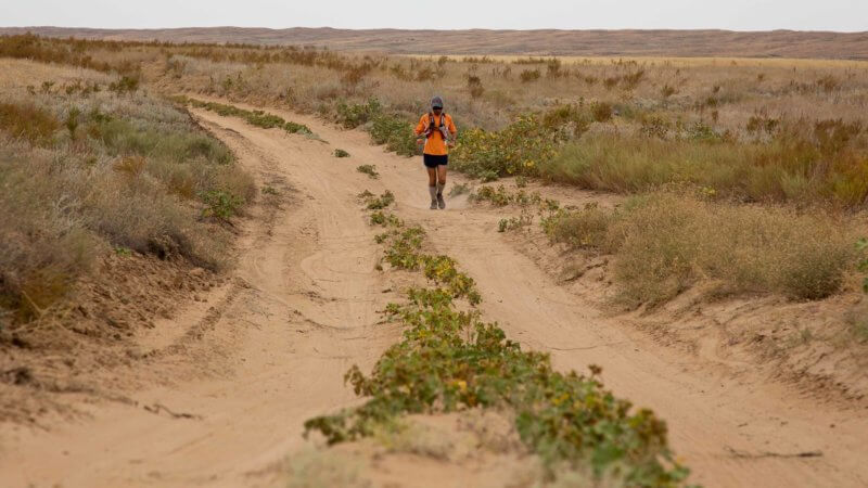 A runner crosses a sandy track in a Kazakhstan desert.