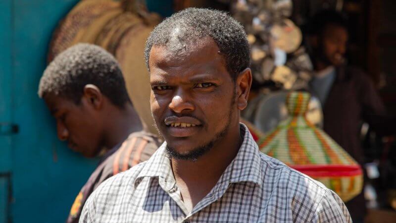 A man with a white and brown checked shirt poses in an Addis Ababa market.