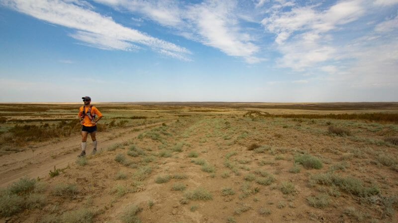 Jamie Maddison, an English ultra runner crossing a flat and wide expanse of desert steppe.