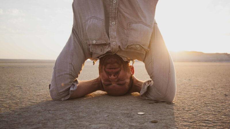 A man wearing a khaki shirt does a handstand and grimaces.