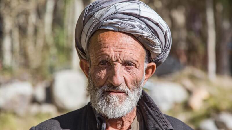Older Wakhan man with hard scarf wrapped around his head and a white beard.