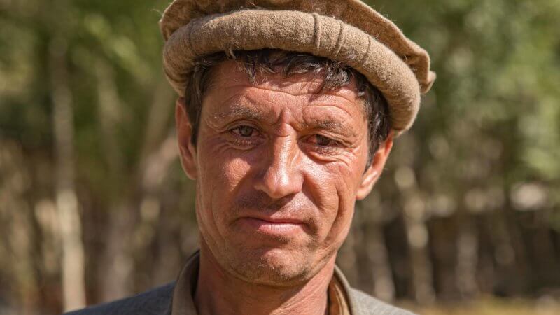 Afghan man with weathered face wearing a pakol hat and looking serious.