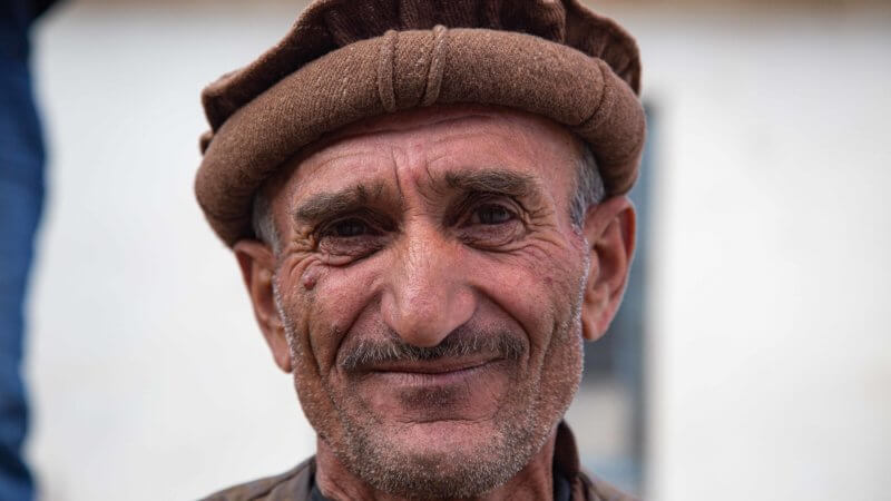 An older man wearing a khaki Afghan pakol hat.