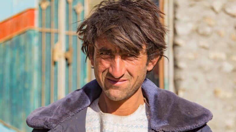A wild haired Afghan man wearing a blue coat looking into the camera.