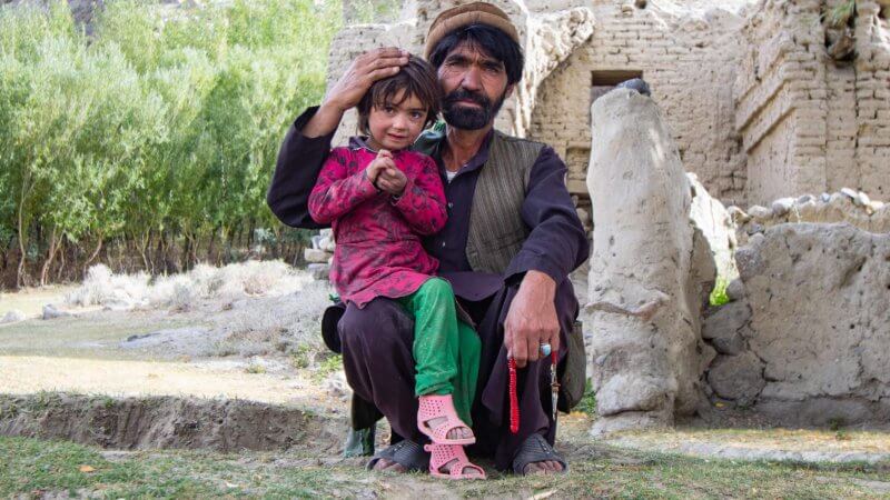 An Afghan man crouching down with his child on his lap.