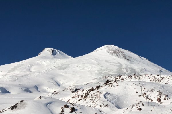 A far shot of the twin peaks of Mount Elbrus in Russia, covered in snow.